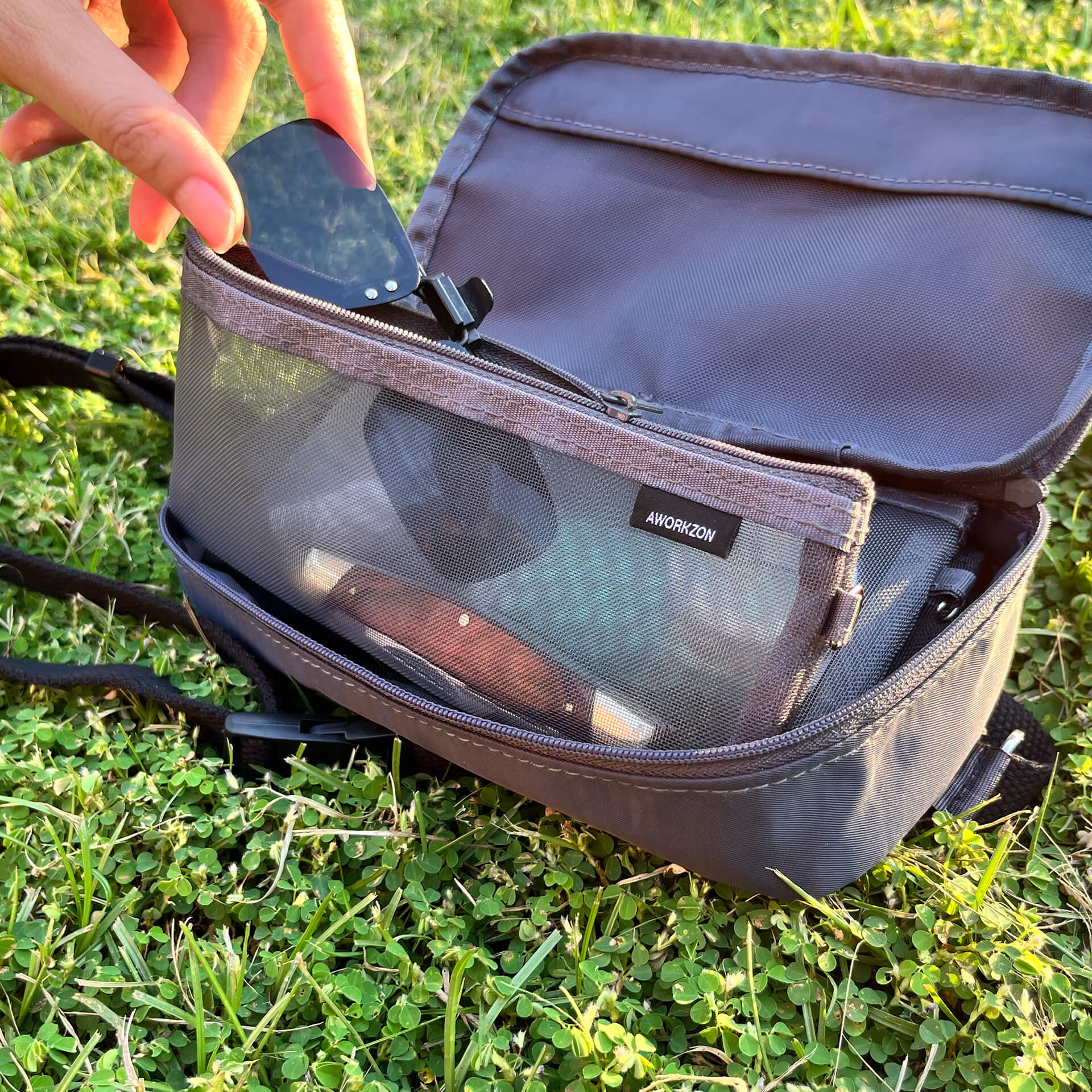 In an outdoor setting, a person opens the 190+ Organizer and takes a pair of sunglasses from one of the mesh bag